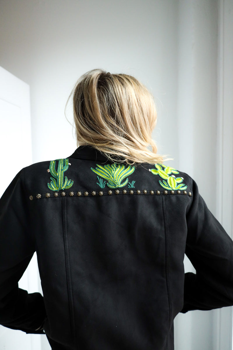 Person wearing a black jacket with green cactus embroidery on the shoulders against a white background