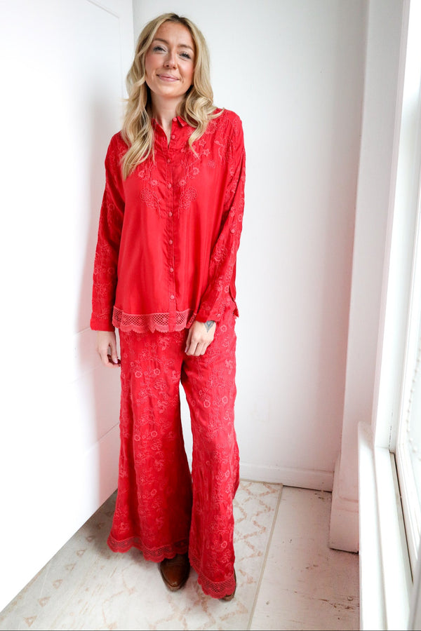 Woman wearing red pajama set standing in a room with white walls and a window.