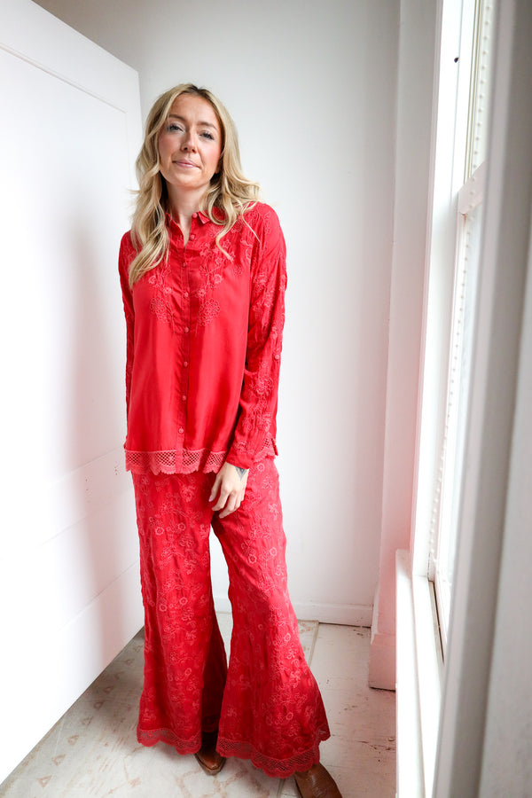 Woman wearing a red lace pajama set standing in a bright room with white walls and a window.