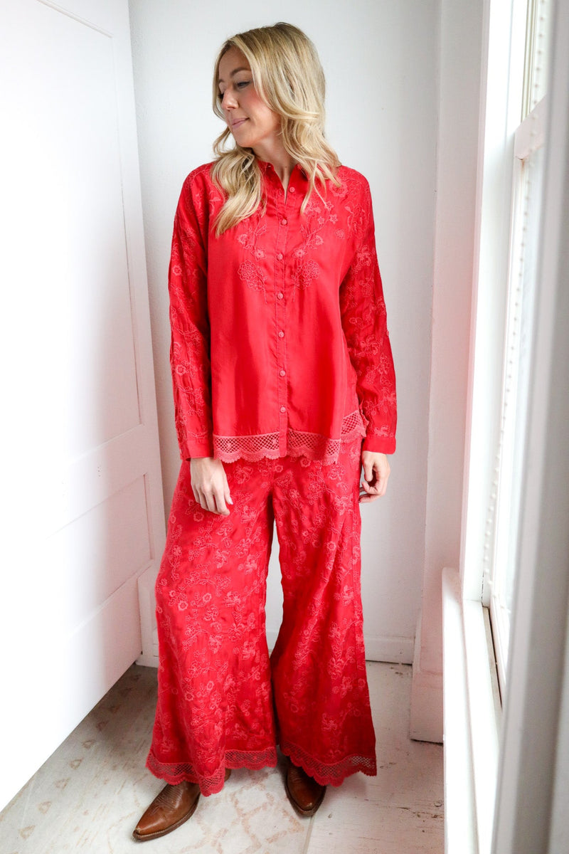 Woman wearing red pajama set standing in a room with white walls and a window.