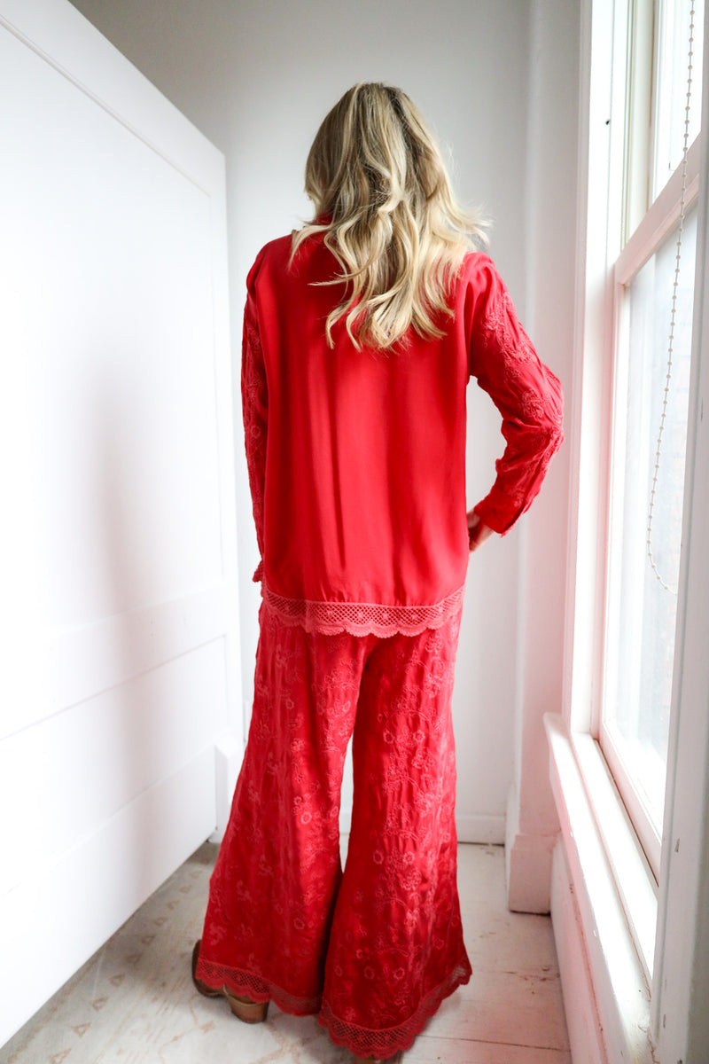 Person wearing a red outfit with lace details standing by a window.