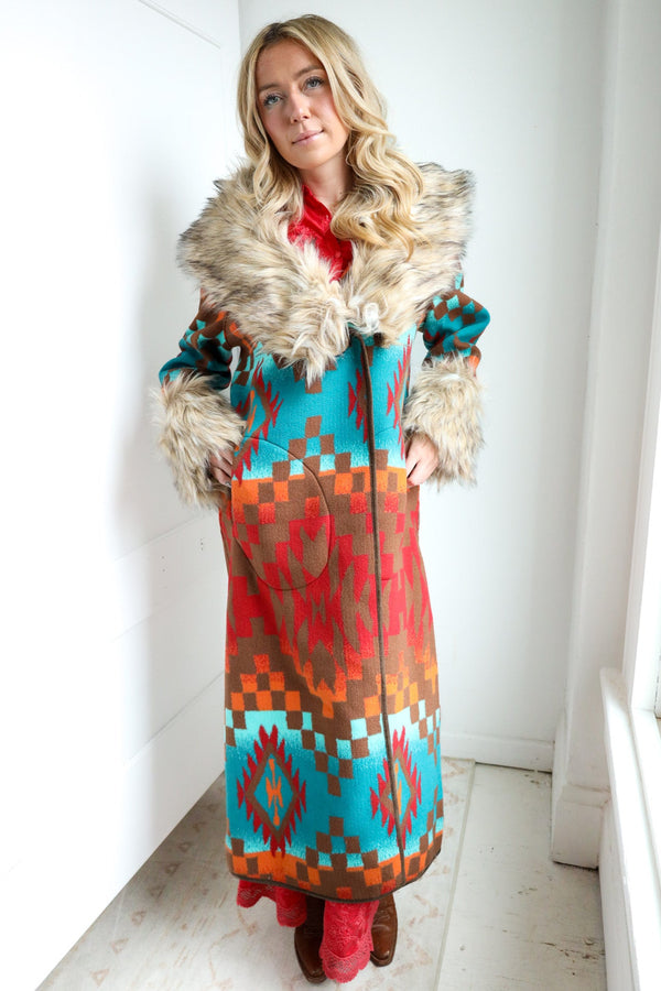 Woman wearing a colorful patterned coat with fur trim indoors.