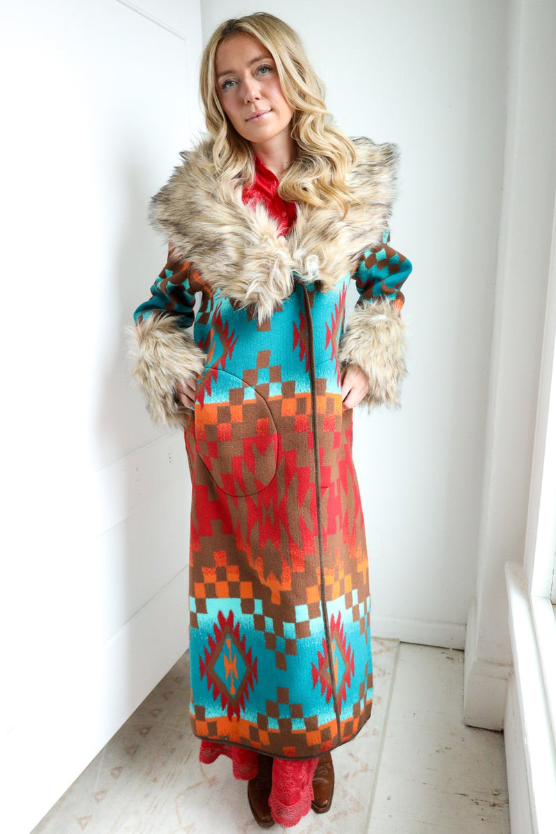 Woman wearing a colorful patterned coat with fur trim indoors.