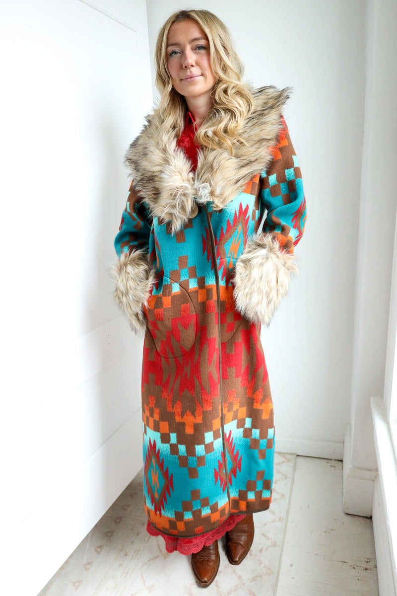 Woman wearing a colorful patterned coat with fur trim indoors.