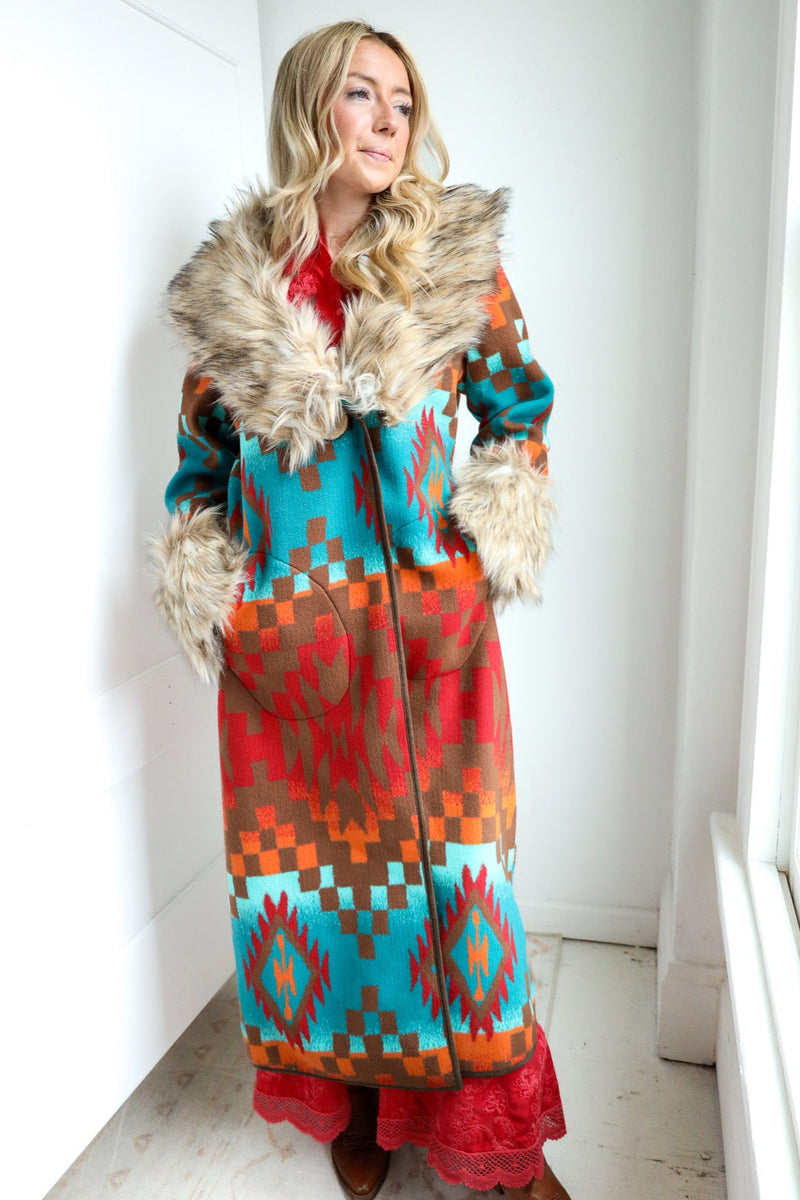 Woman wearing a colorful patterned coat with fur trim indoors.