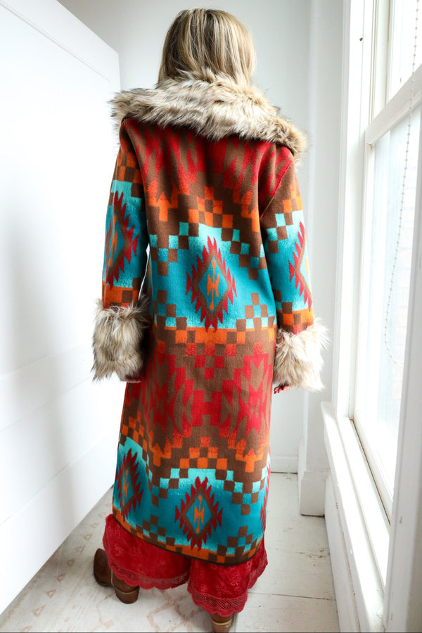 Person wearing a colorful patterned coat with fur trim in a bright room.
