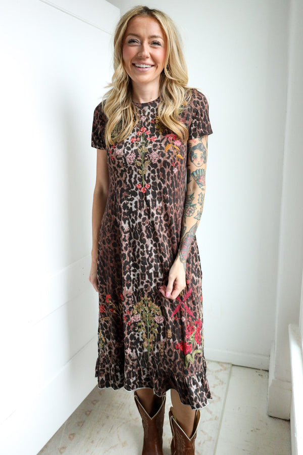 Woman wearing a patterned dress standing against a white wall.