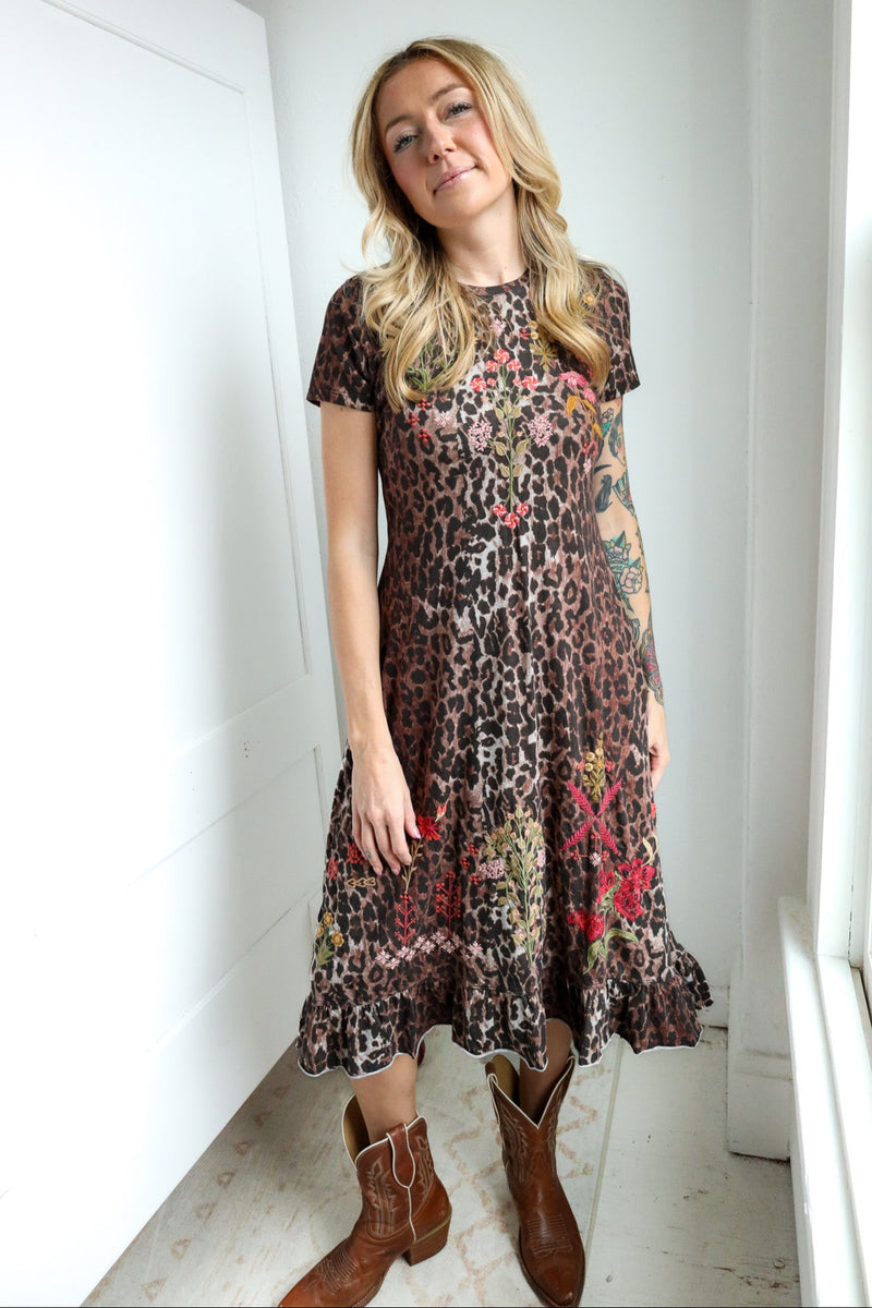 Woman wearing a patterned dress with floral and leopard print elements, standing indoors.