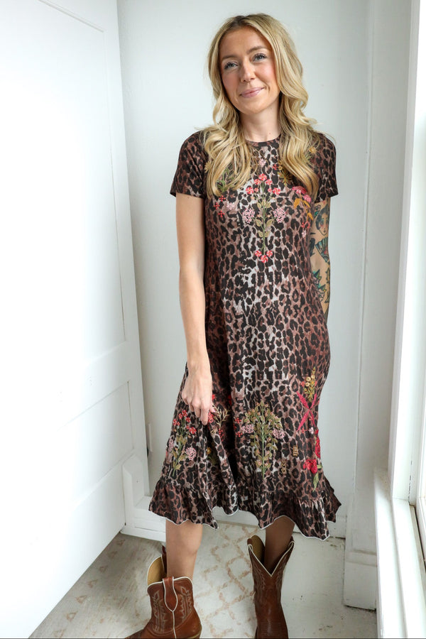 Woman wearing a floral and leopard print dress standing in a room with white walls and a window.