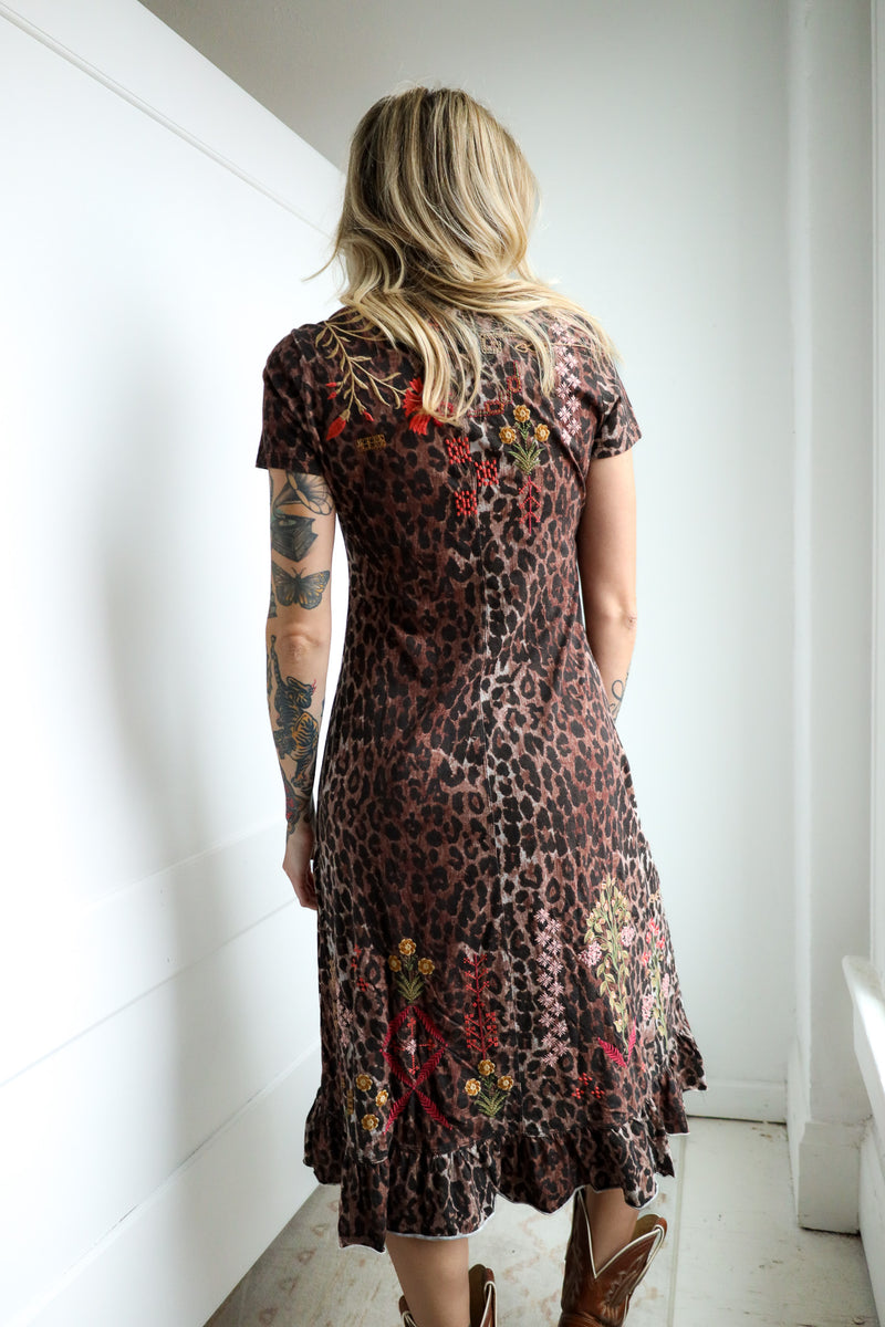 Woman wearing a leopard print dress with floral embroidery in a minimal indoor setting.