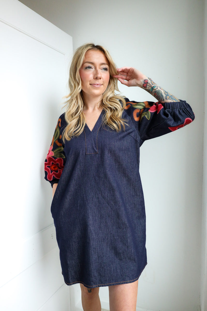 Woman wearing a navy dress with colorful sleeves against a white wall