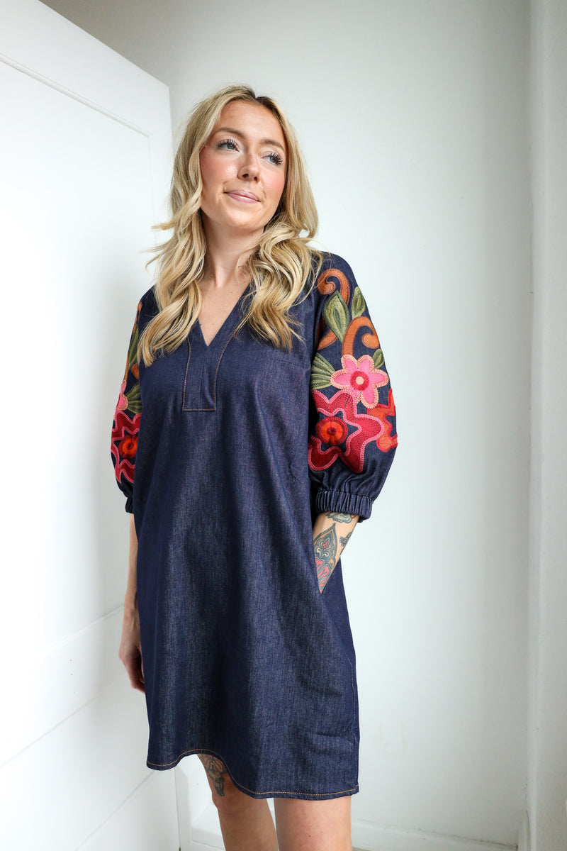 Woman wearing a blue dress with colorful floral sleeves against a white background