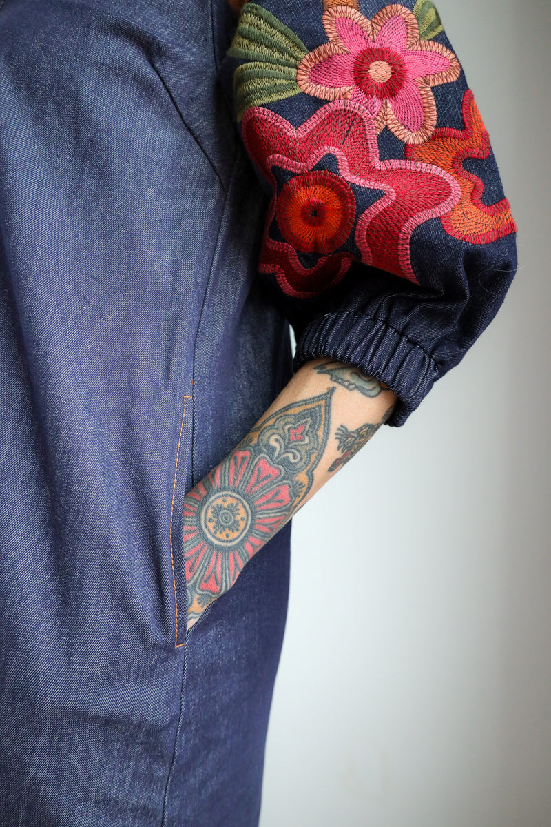 Close-up of a denim jacket with a colorful embroidered sleeve and tattooed arm.