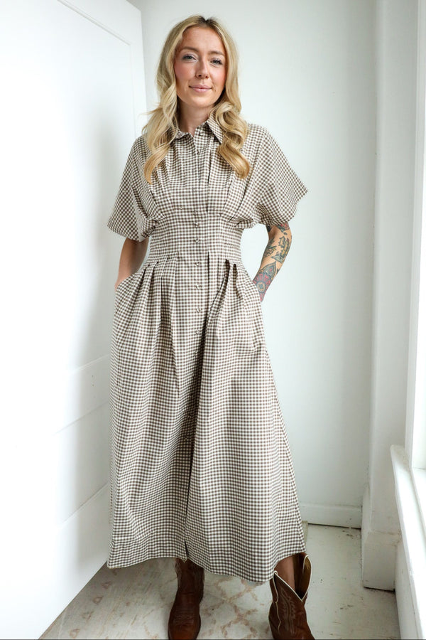 Woman wearing a checkered dress standing in a room with white walls and a light-colored floor.