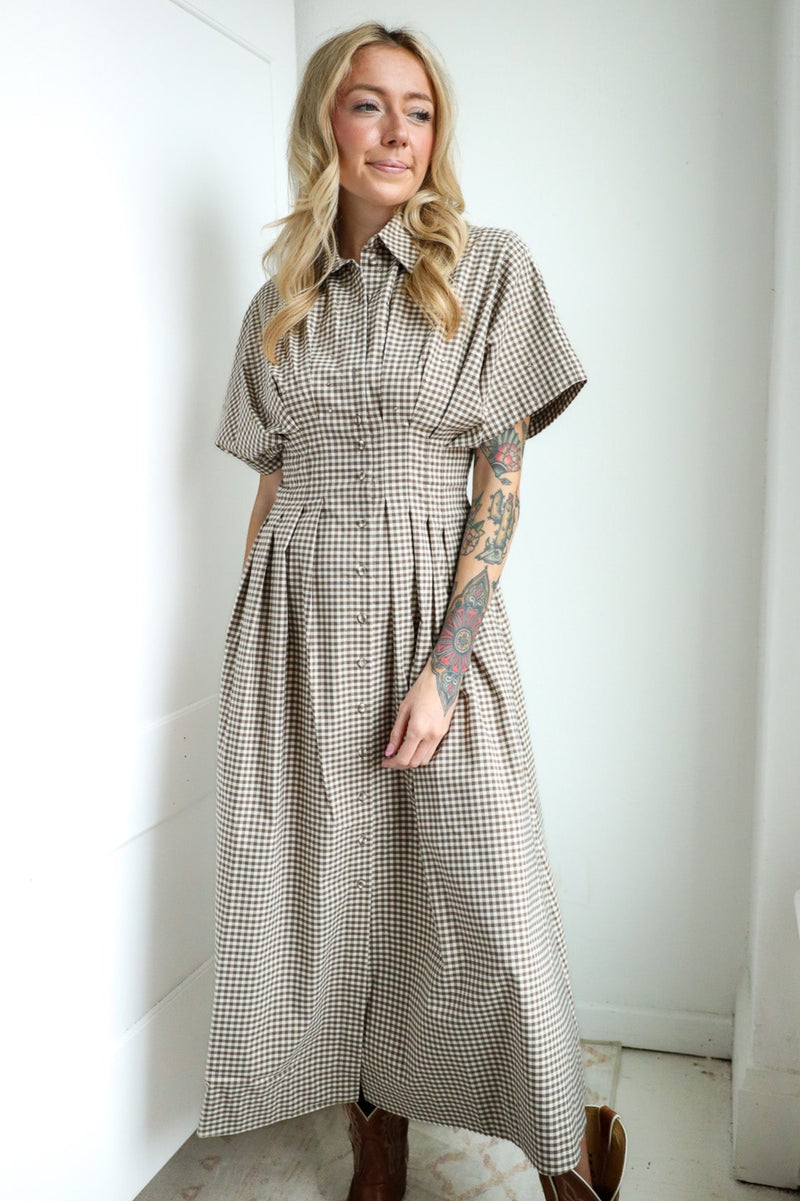 Woman wearing a checkered dress standing in a bright room with white walls.