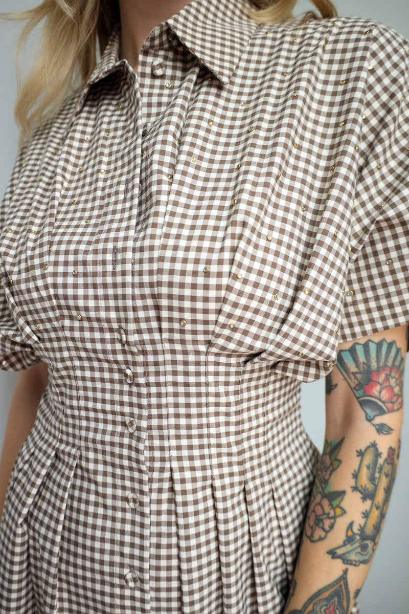 Person wearing a brown and white checkered dress with a tattooed arm.