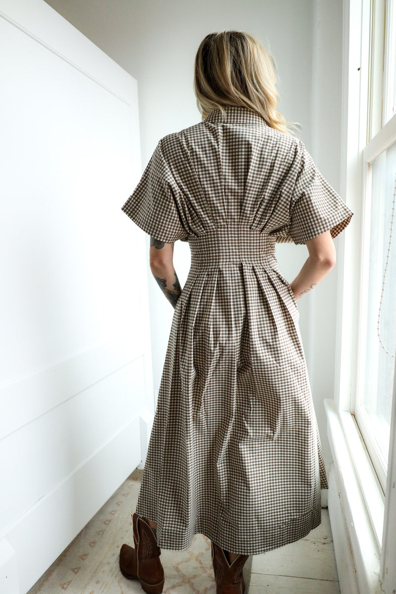 Person wearing a checkered dress standing by a window in a bright room.