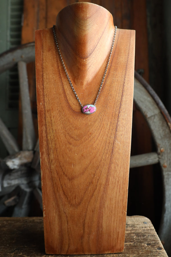 Necklace with a pink pendant on a wooden stand against a rustic background
