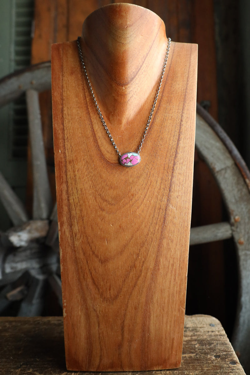 Necklace with a pink pendant on a wooden stand against a rustic background