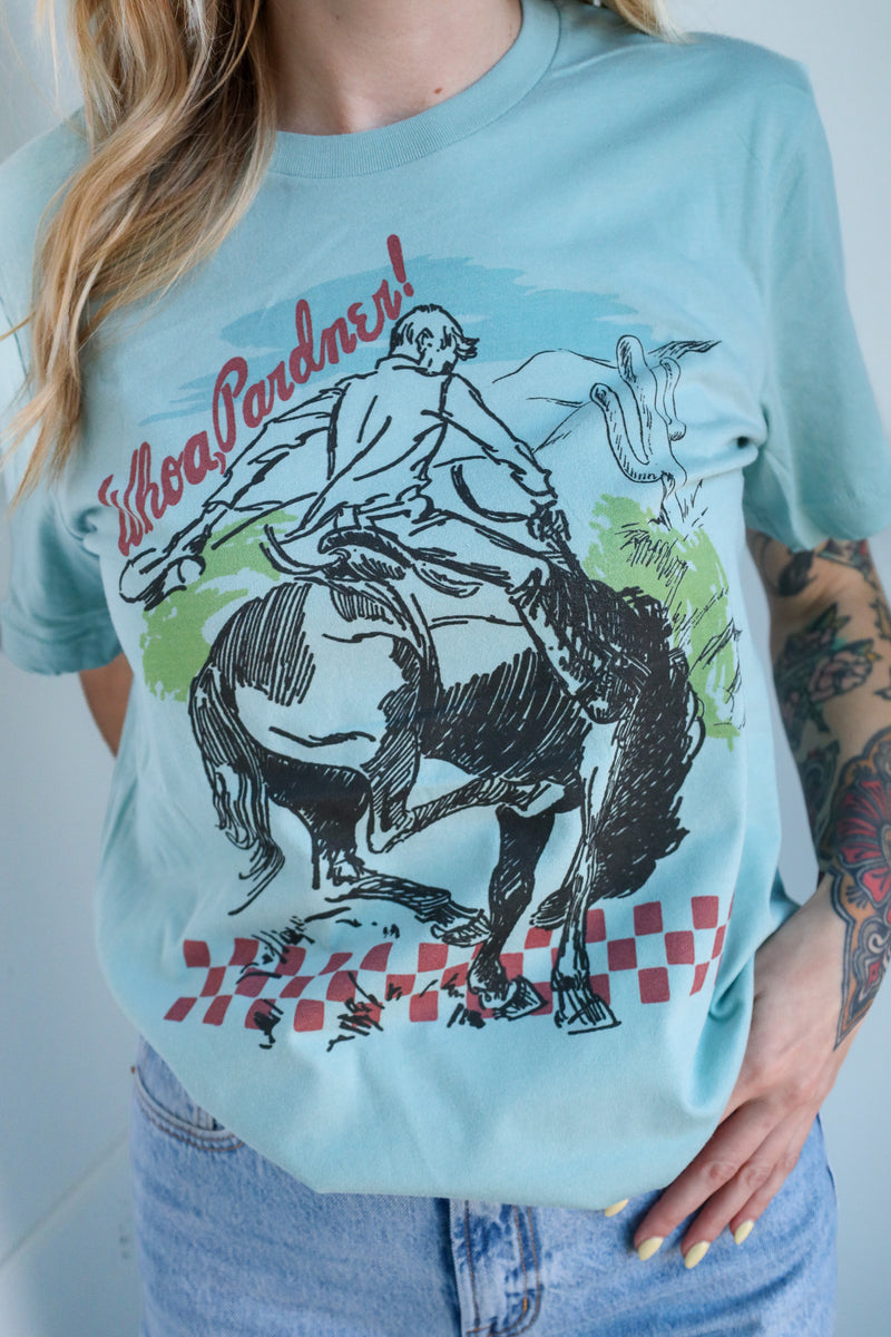 Person wearing a light blue t-shirt with a graphic design of a person riding a horse and text.