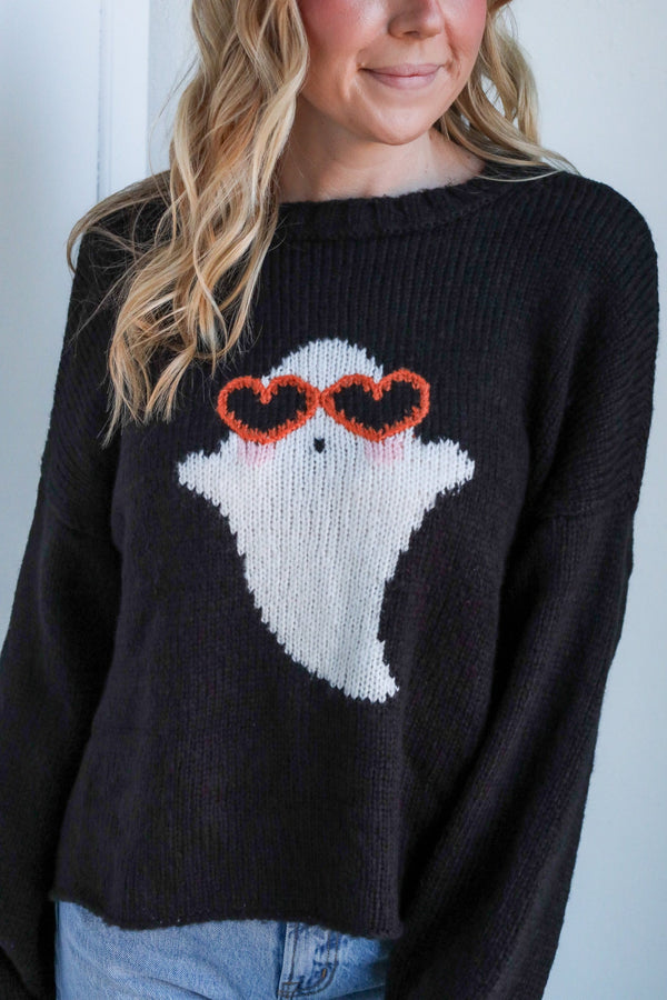 Person wearing a black sweater with a ghost design and heart sunglasses.