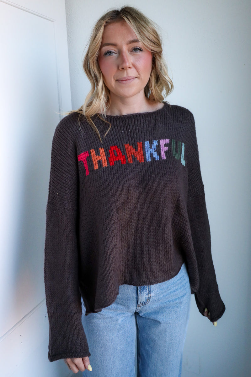 Person wearing a dark sweater with 'THANKFUL' in colorful letters against a light background