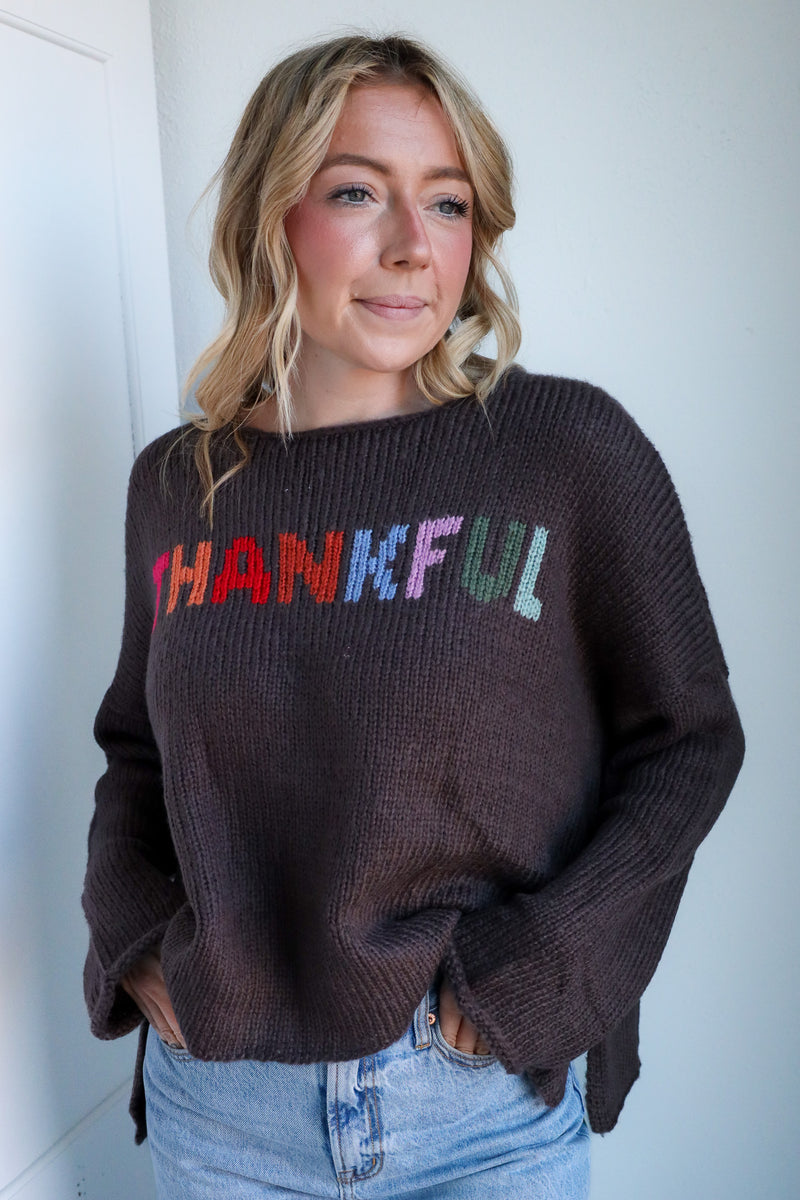 Woman wearing a brown sweater with 'THANKFUL' in colorful letters against a white background