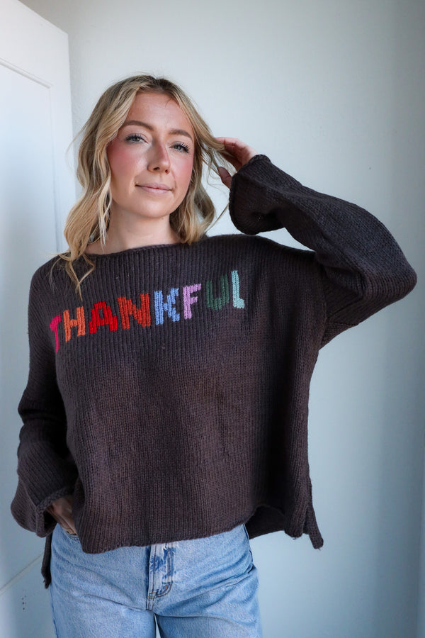 Person wearing a sweater with 'THANKFUL' in colorful letters against a plain background