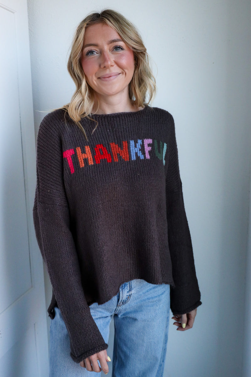Person wearing a dark sweater with 'THANKFUL' in colorful letters against a plain background