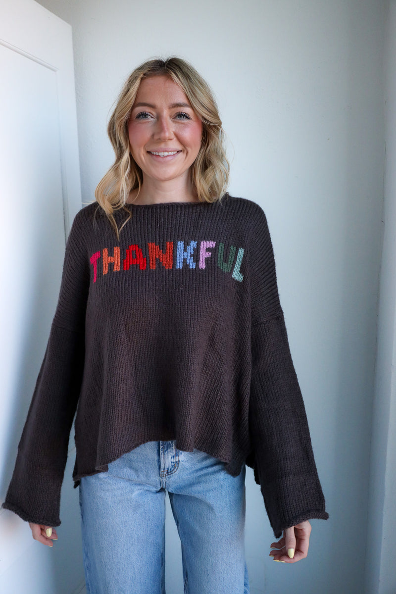 Woman wearing a black sweater with 'THANKFUL' in colorful letters against a plain background
