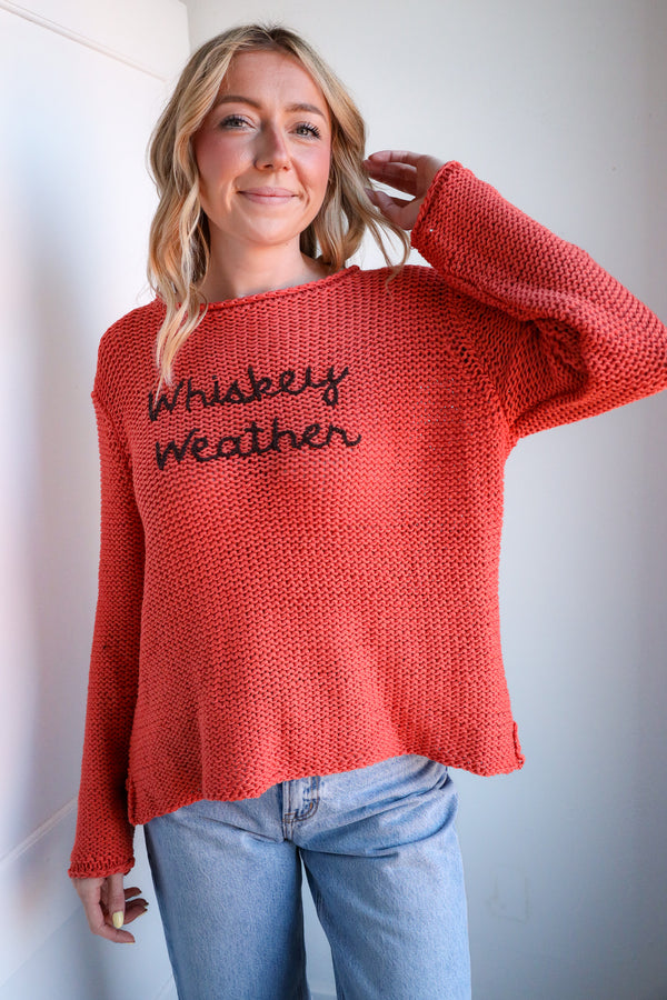 Woman wearing a red sweater with 'Whiskey Weather' text against a plain background