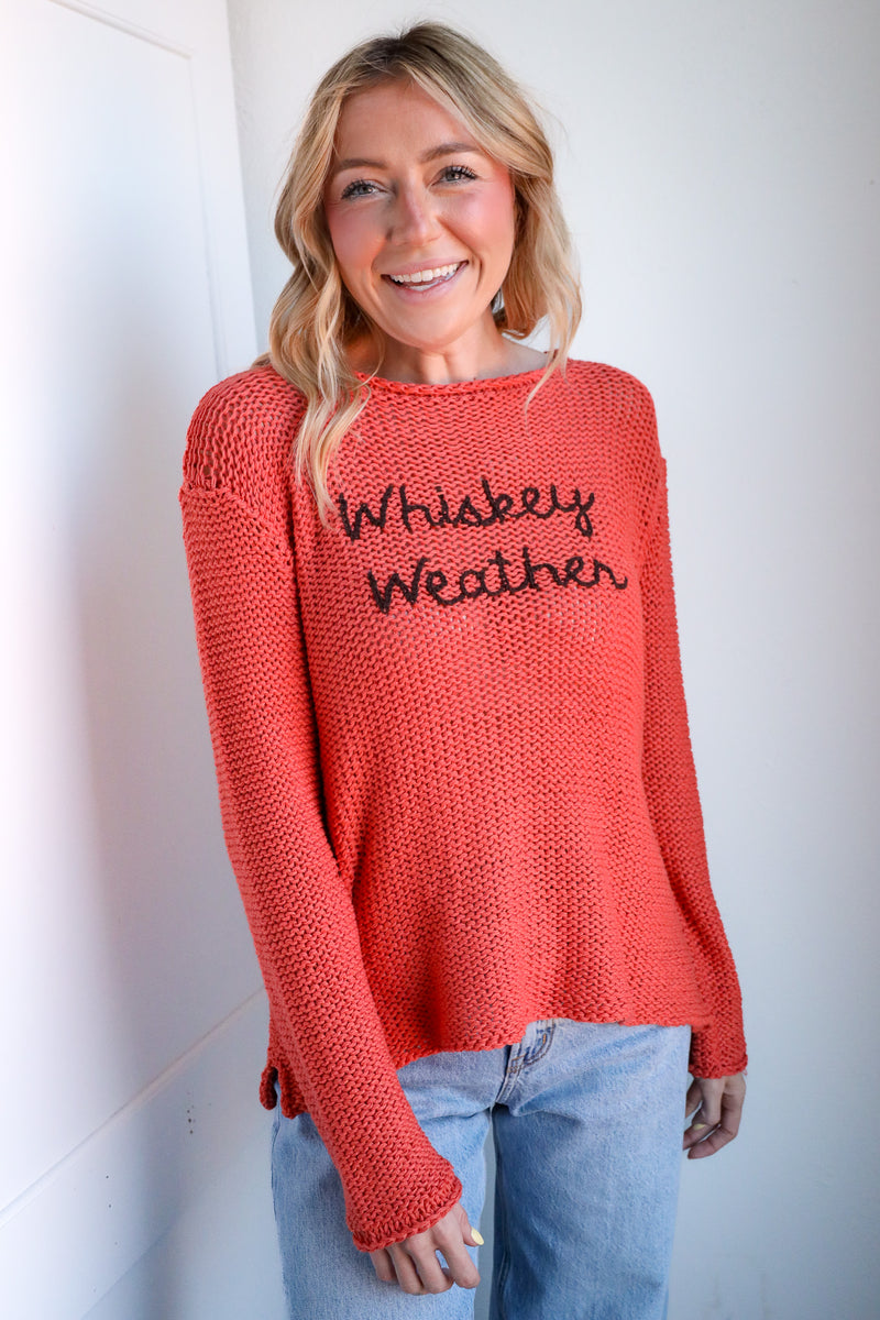 Woman wearing a red sweater with 'Whiskey Weather' text against a white wall