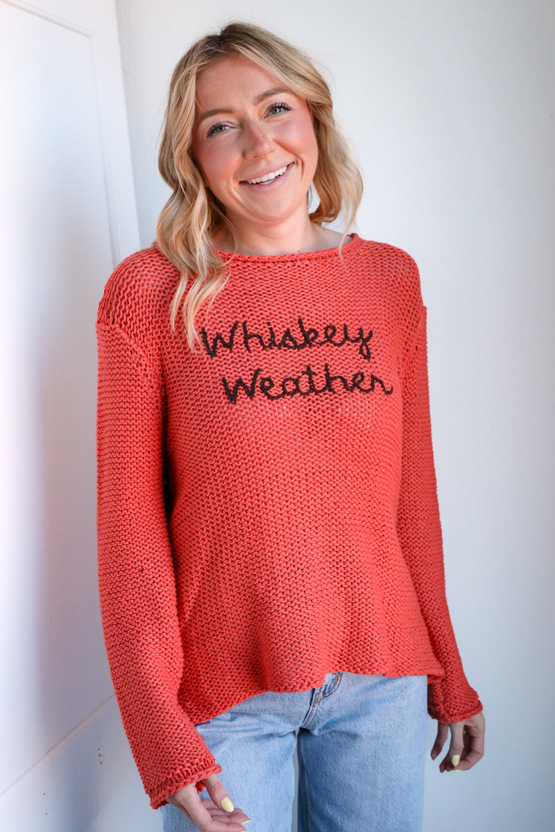 Woman wearing a red sweater with 'Whiskey Weather' text against a white wall