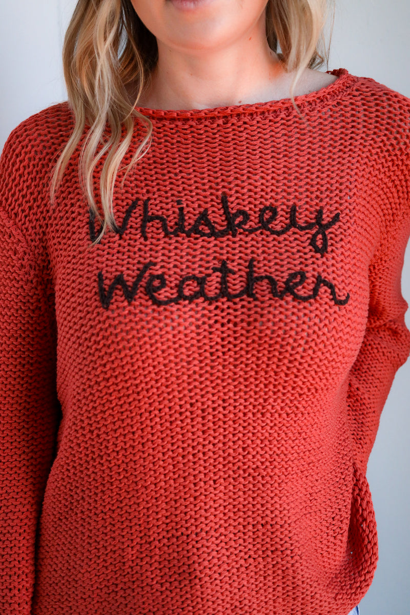 Red knitted sweater with 'Whiskey Weather' text on a plain background