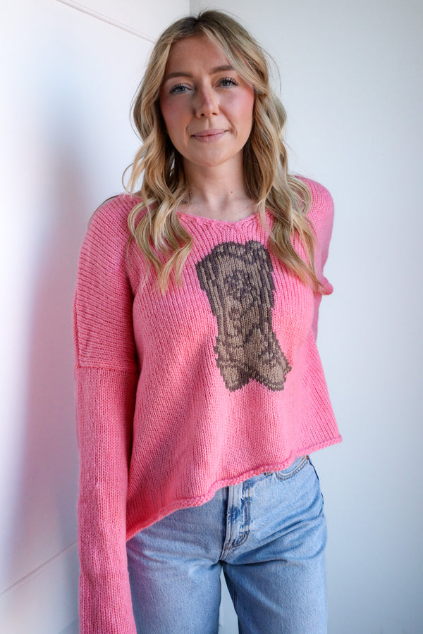 Woman wearing a pink sweater with a graphic design against a white wall