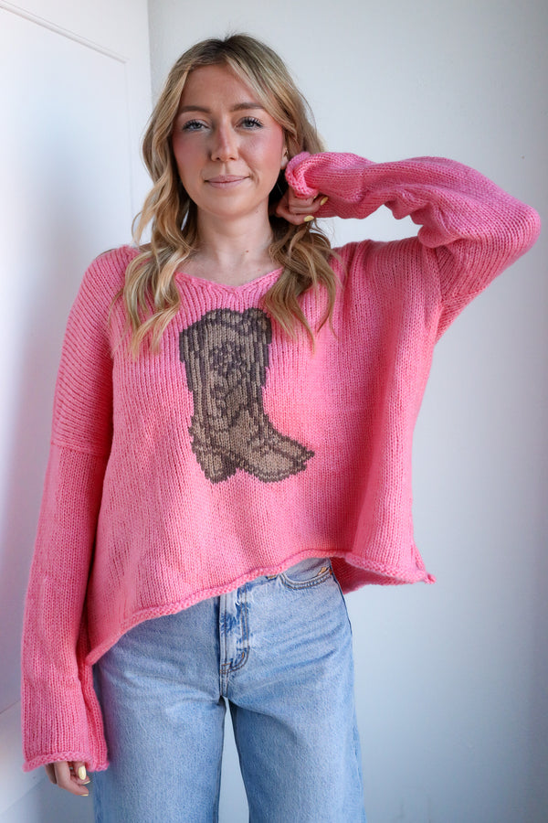 Person wearing a pink sweater with a lace boot design, standing against a plain background.