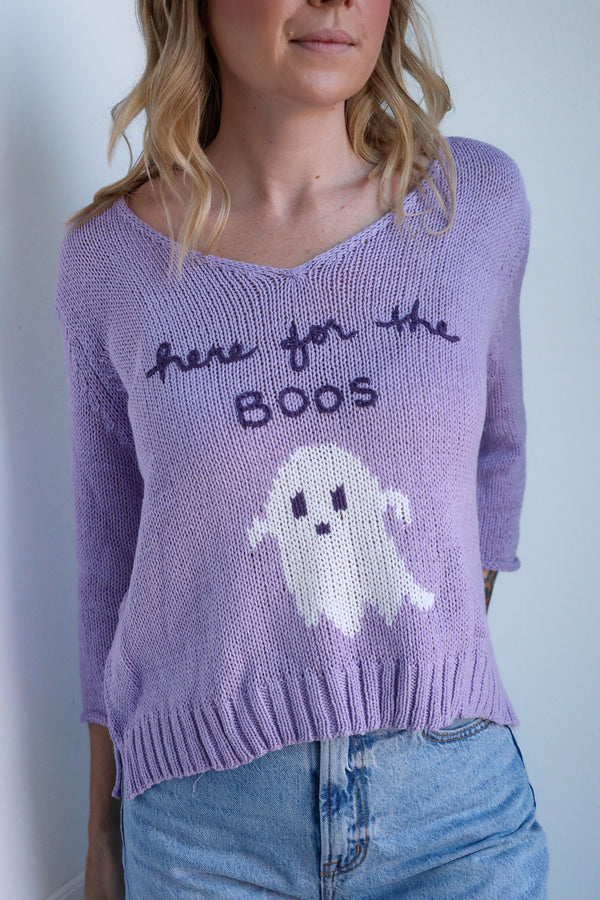 Person wearing a purple sweater with a ghost and text design against a plain background