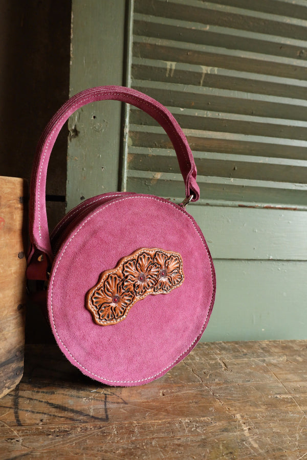 Purse crafted from mauve roughout leather, this purse features a beautiful circle design with a floral tooled front. Its matching handle and zipper closure provide convenience, while the twin interior pockets offer ample storage.