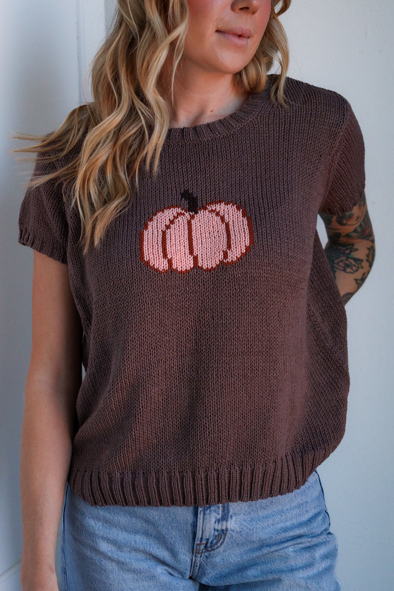 Woman wearing a brown sweater with pink pumpkin design against a white background
