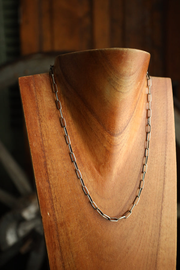 Silver chain necklace on a wooden stand with a blurred background