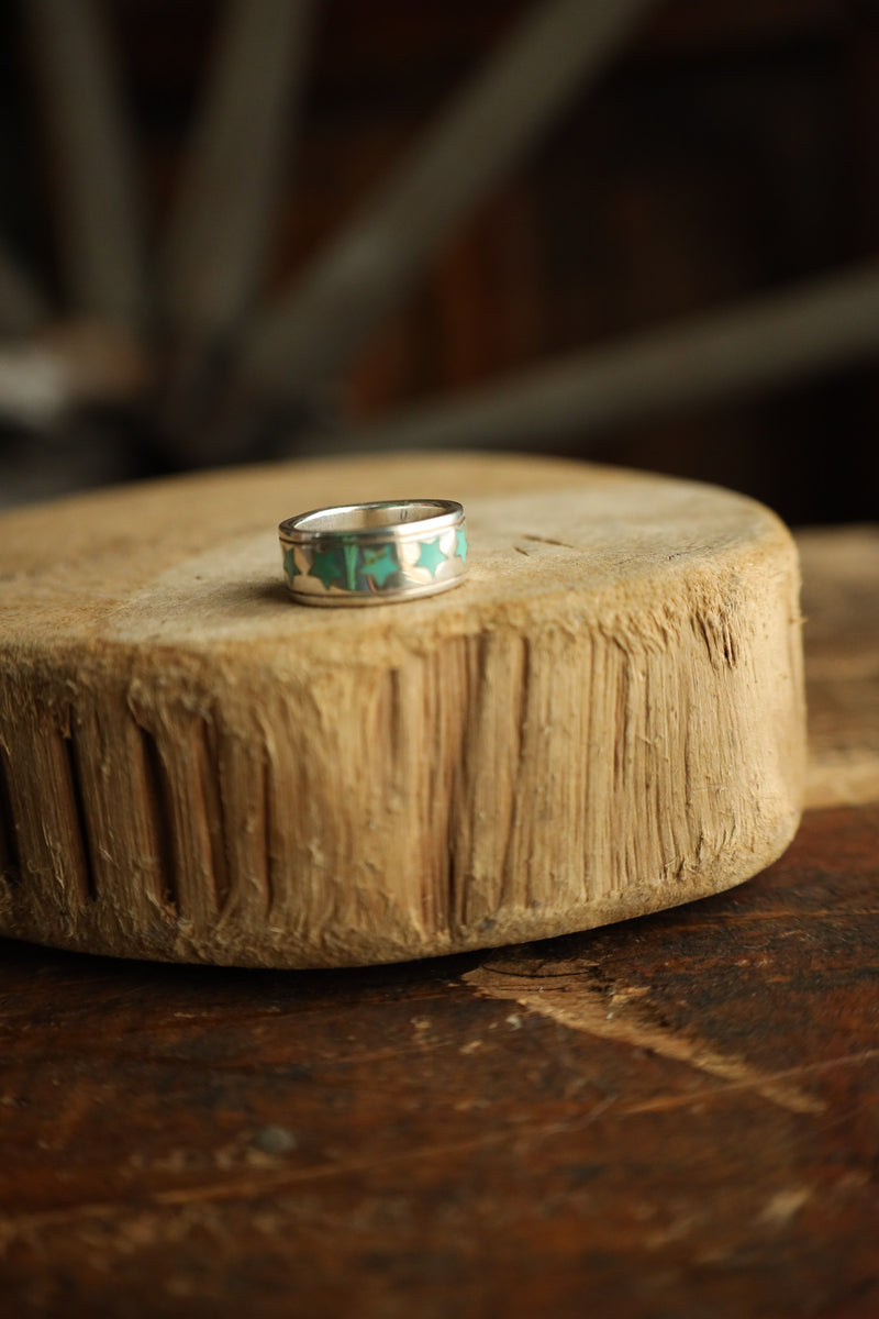 Silver ring with green inlay on a wooden surface