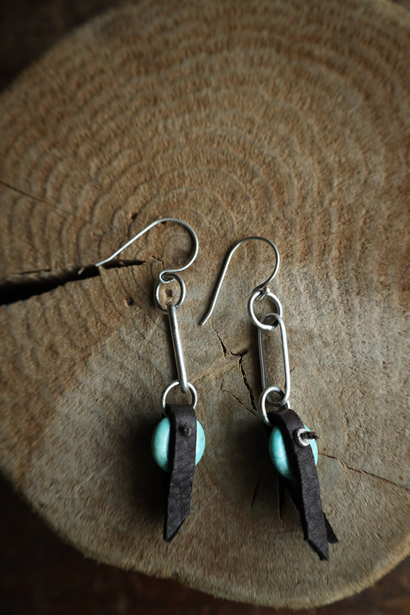 Pair of earrings with turquoise beads and feather-like pendants on a wooden surface