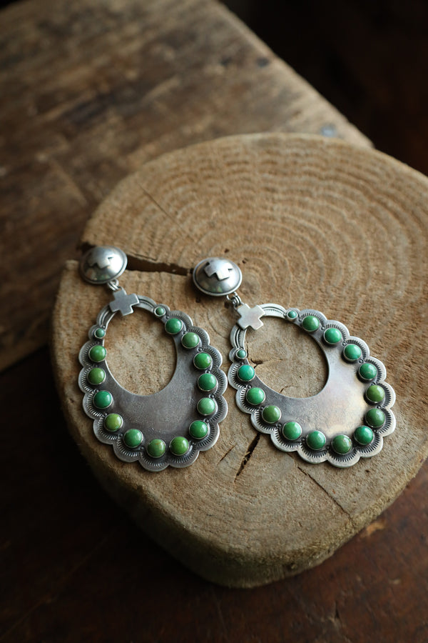 Silver hoop earrings with green beads on a wooden surface