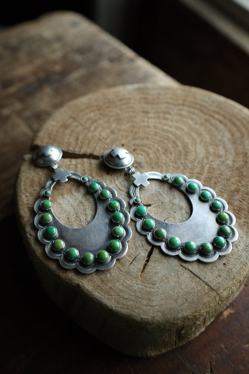 Silver earrings with green beads on a wooden block