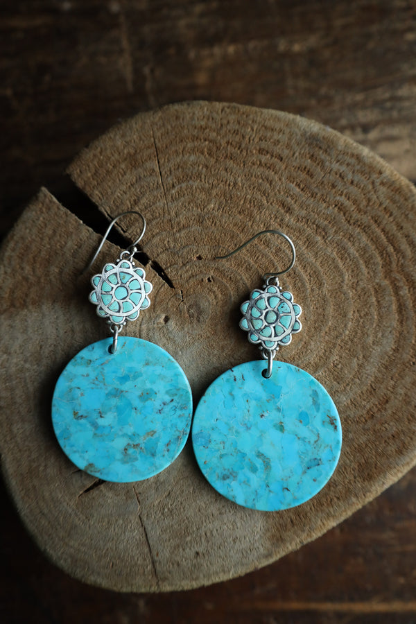 Turquoise earrings with silver floral tops on a wooden surface