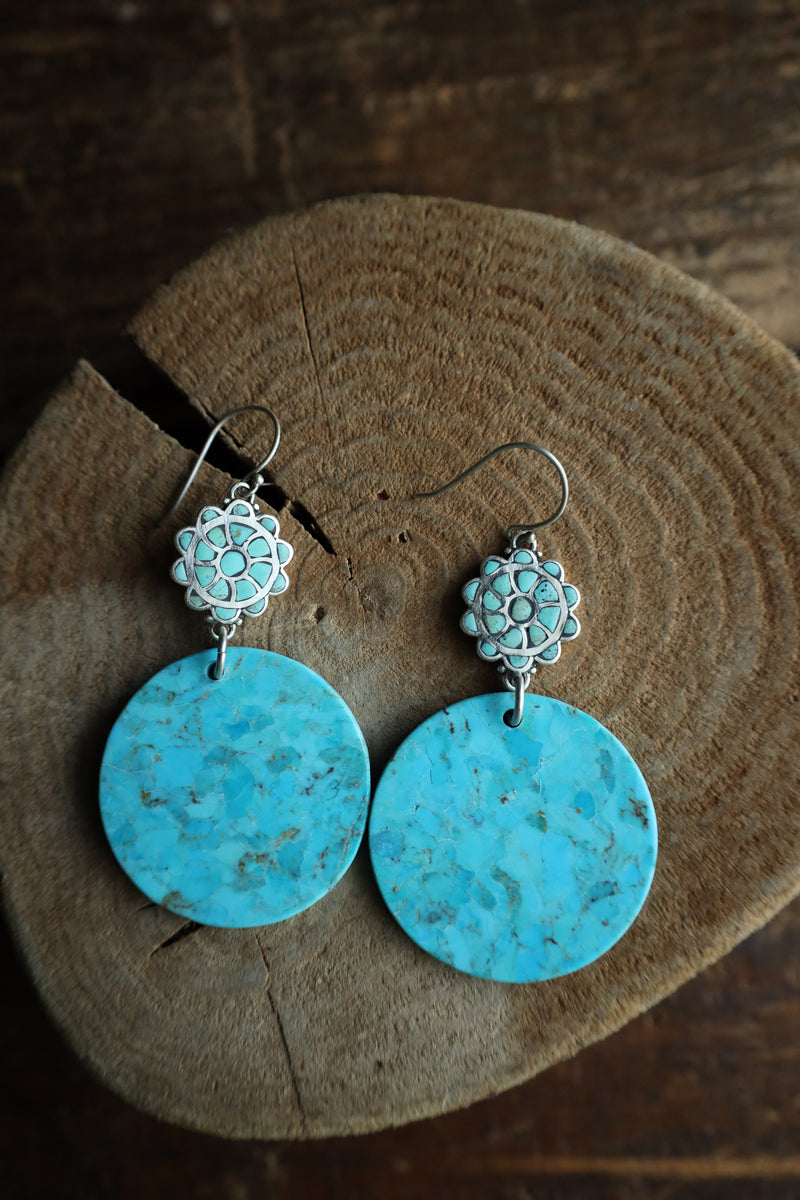 Turquoise earrings with silver floral tops on a wooden surface