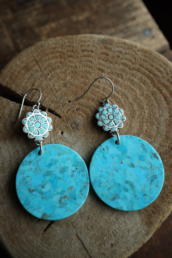 Turquoise earrings with silver floral tops on a wooden surface