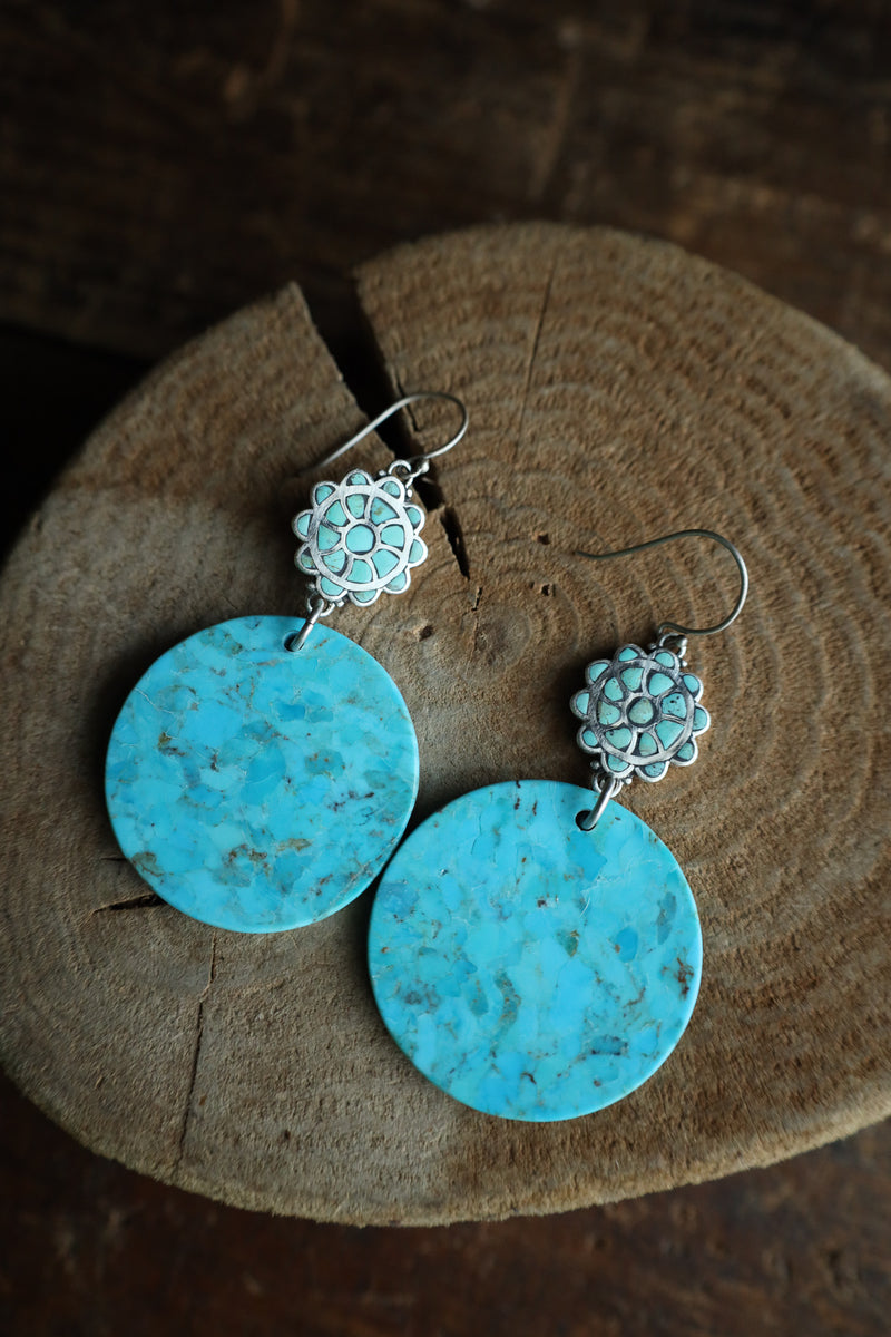 Turquoise earrings with floral tops on a wooden surface