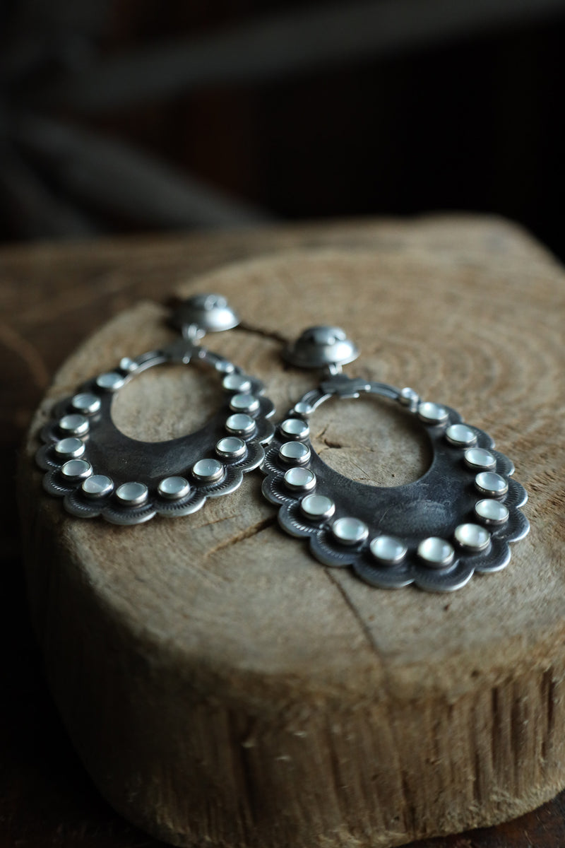 Silver hoop earrings on a wooden block with a dark background