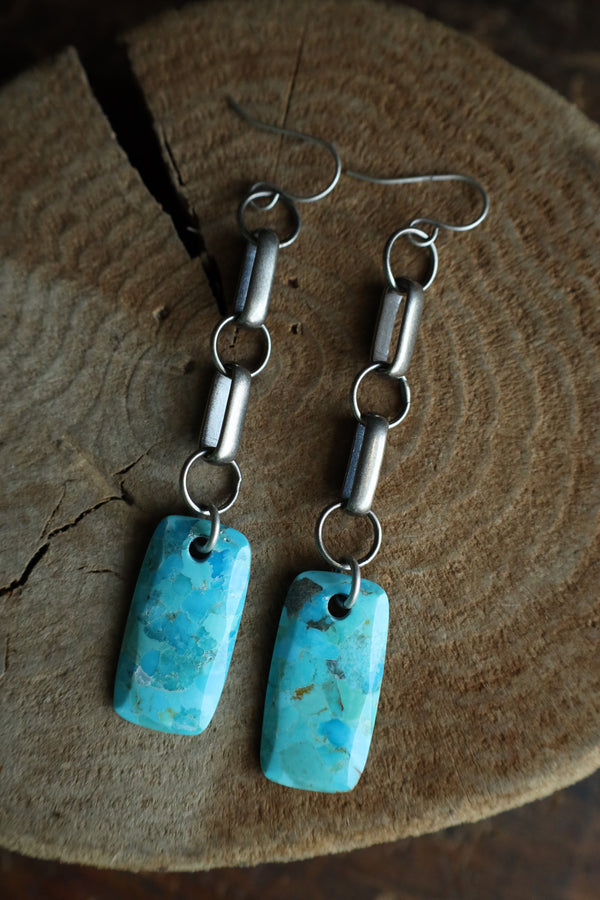 Turquoise earrings with silver chain on a wooden surface